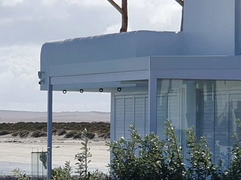 Pale grey curved aluminium canopy with recessed downlights over the glazed corner of a beach house