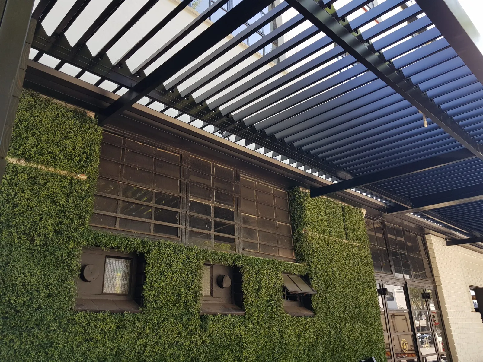 Charcoal louvre awning over a restaurant frontage with a green creeper wall